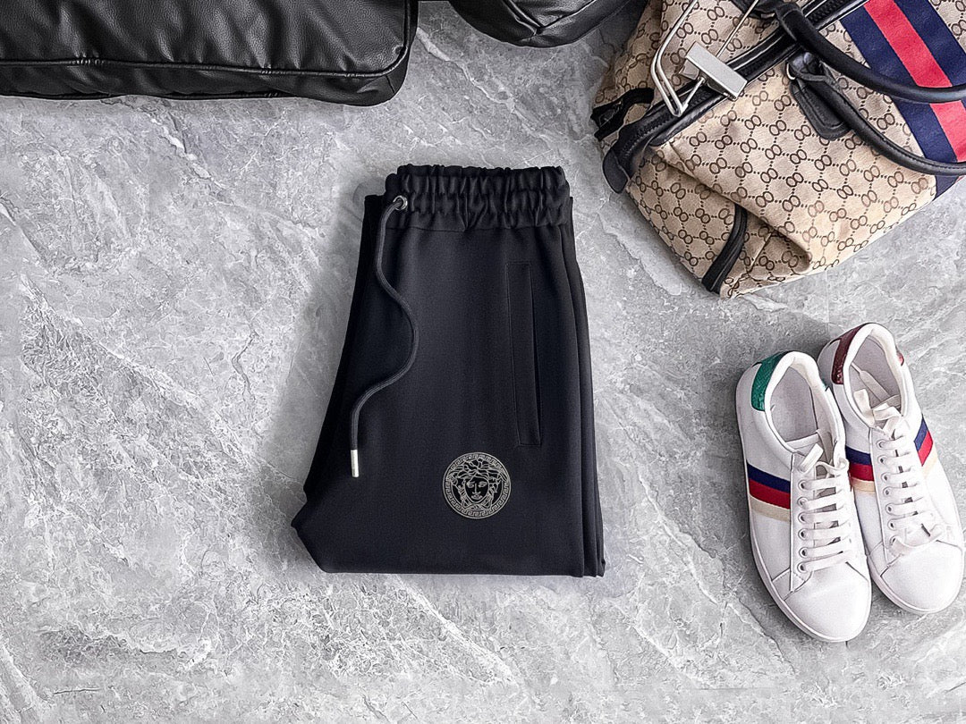 Black jogger pants with elastic waistband, drawstring, and circular logo patch