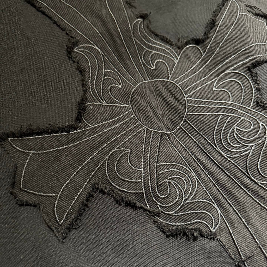 Embroidered cross flower design on black T-shirt fabric with textured stitching