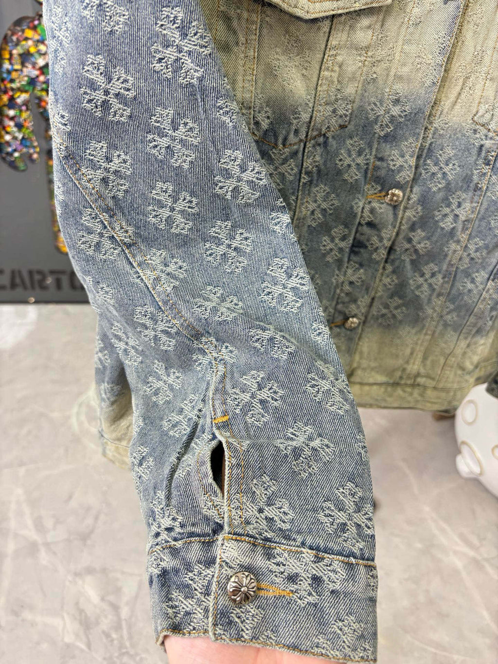 Denim jacket sleeve in blue patterned wash, visible stitched seams and pocket edge