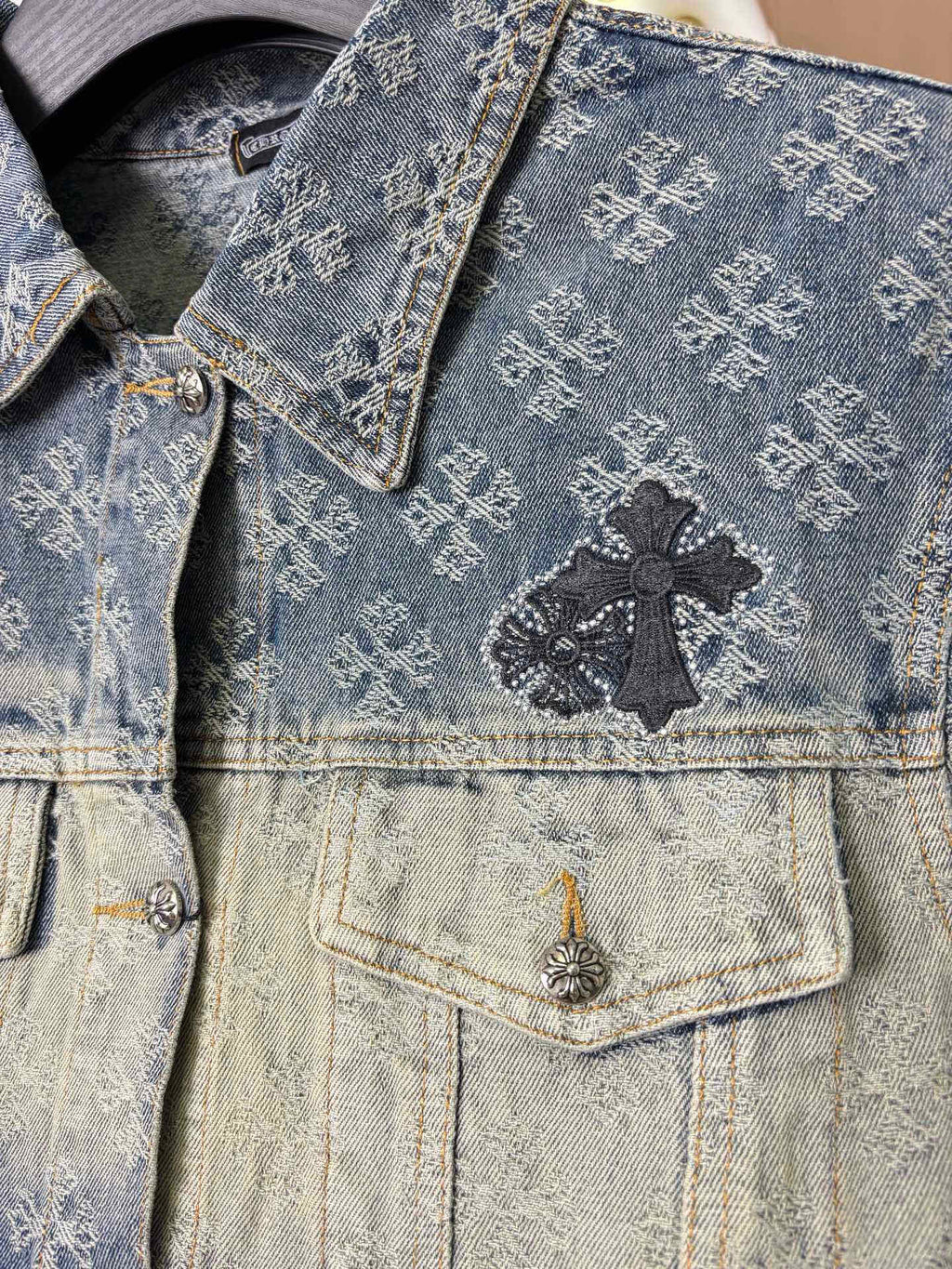 Denim jacket close-up, blue patterned wash, black cross patch on chest pocket