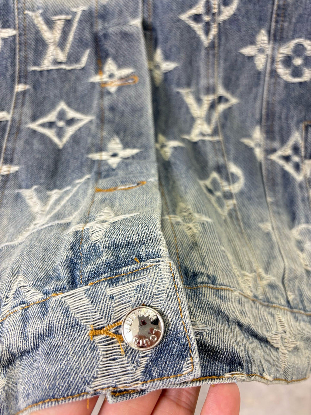 Louis Vuitton denim jacket sleeve and hem close-up with gold monogram print and metal button.