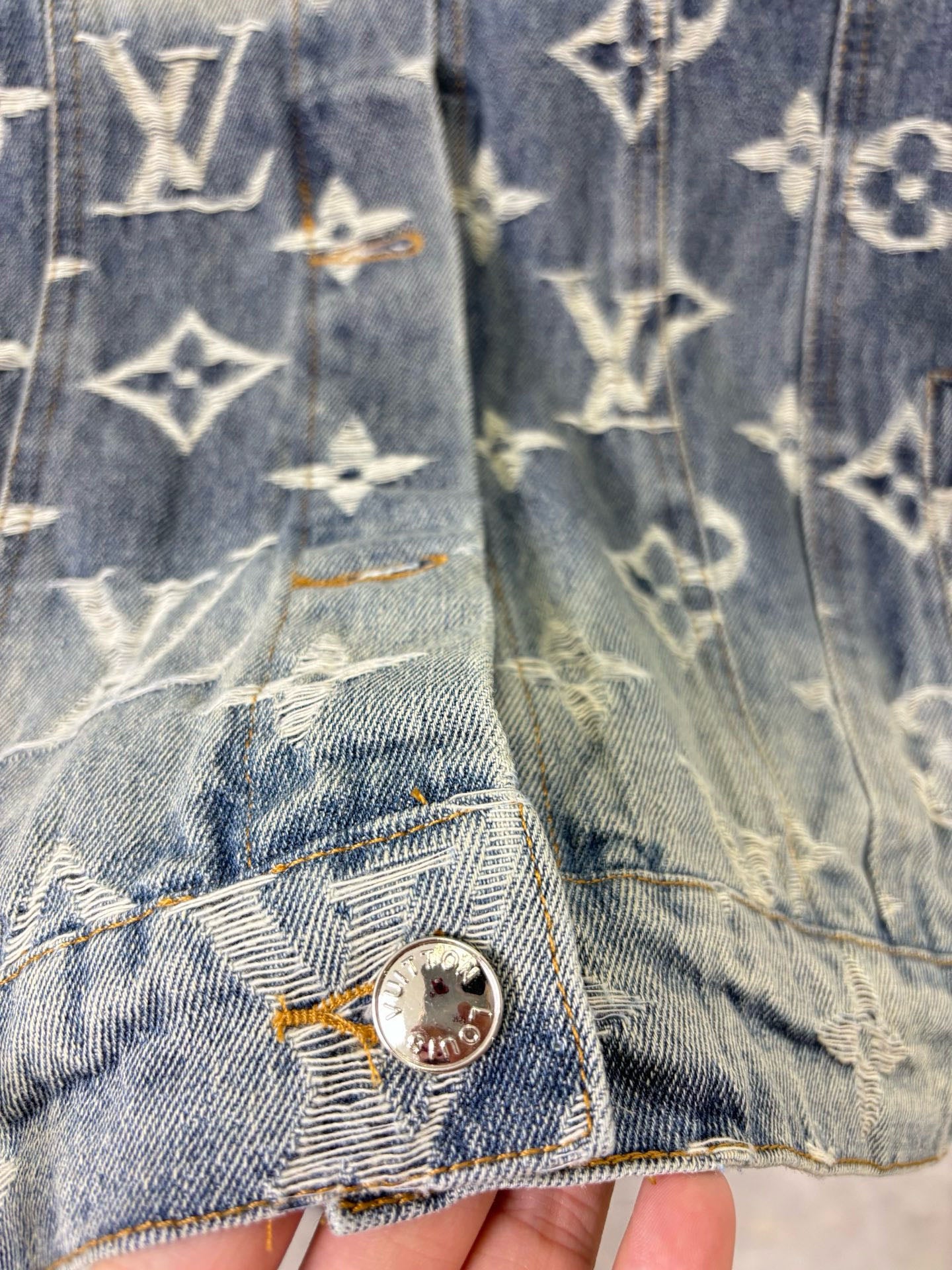 Louis Vuitton denim jacket sleeve and hem close-up with gold monogram print and metal button.