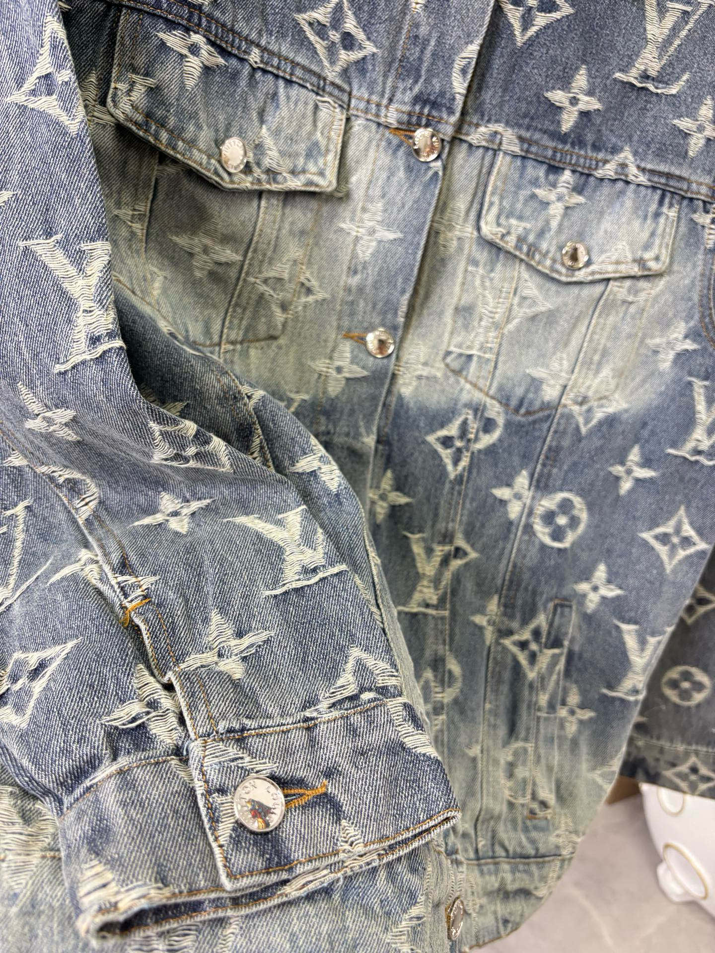 Louis Vuitton denim jacket detail close-up with gold monogram pattern and buttoned flap pockets.