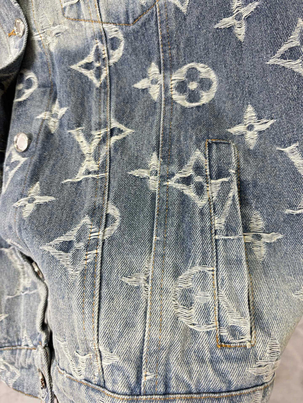Louis Vuitton denim jacket lower body close-up with gold monogram pattern and button trim.