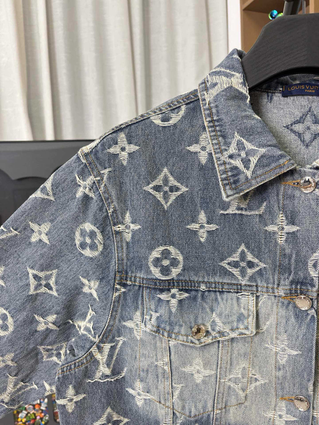 Louis Vuitton denim jacket shoulder and chest close-up with gold monogram print and pocket flap.