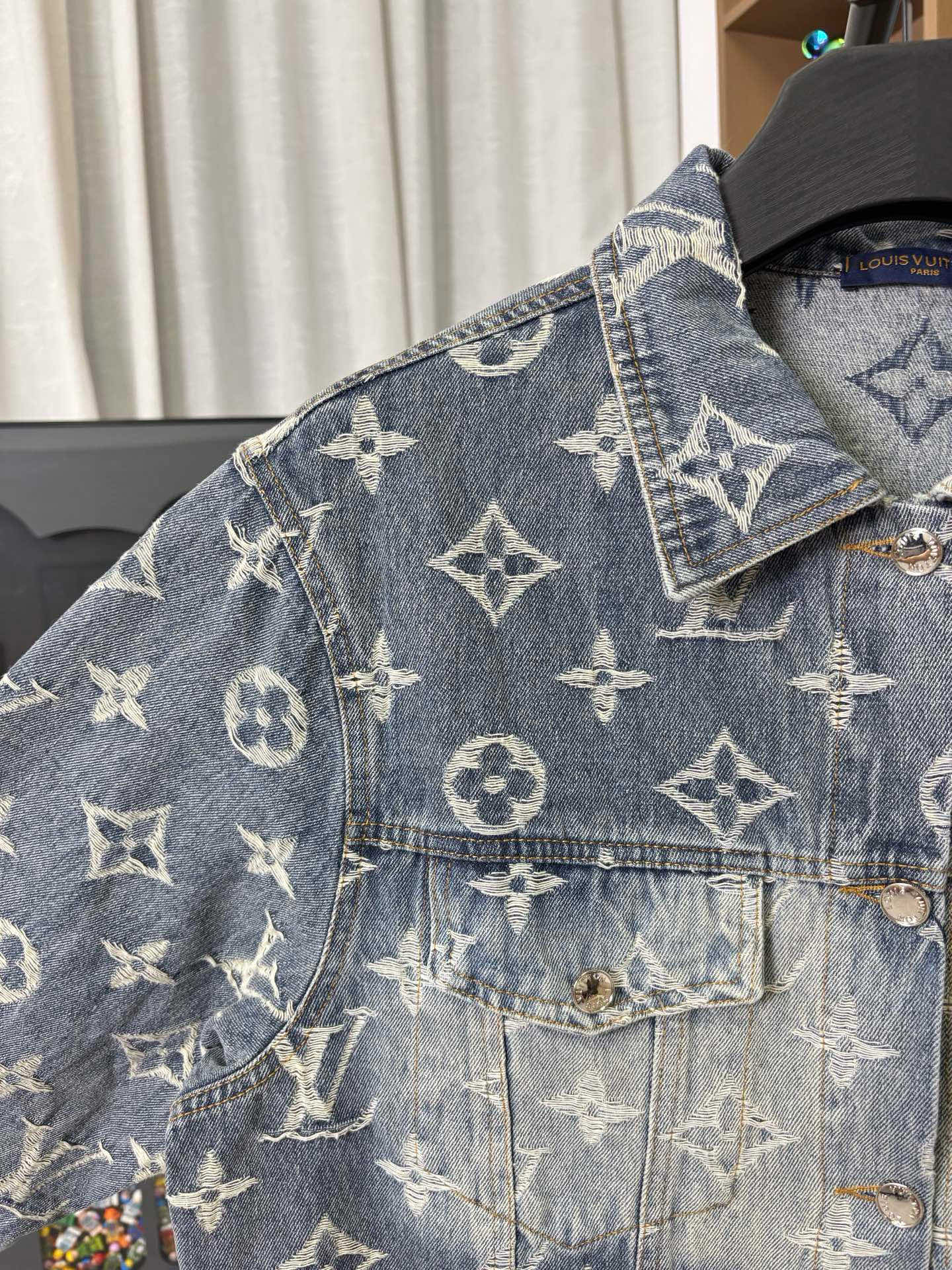 Louis Vuitton denim jacket shoulder and chest close-up with gold monogram print and pocket flap.