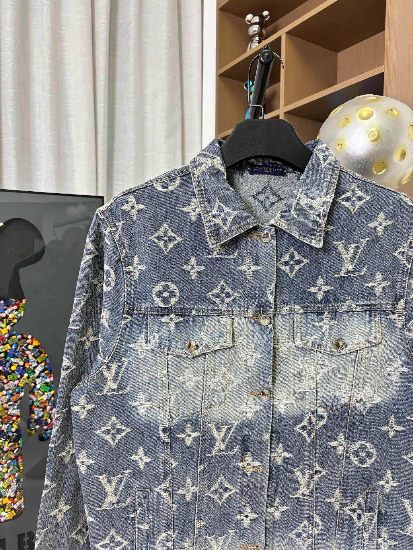 Louis Vuitton denim jacket close-up of chest with gold monogram pattern and buttoned pockets.