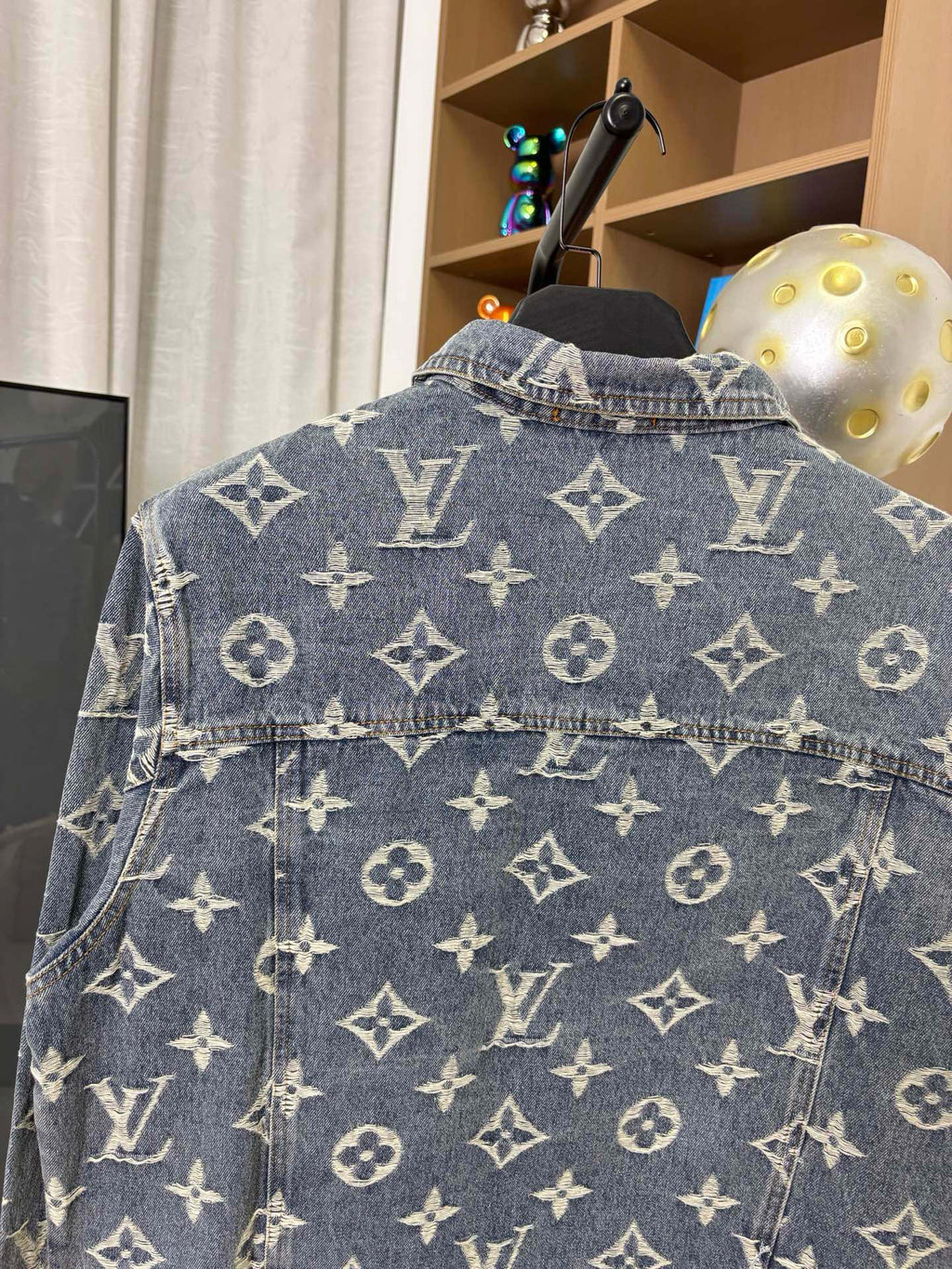Louis Vuitton denim jacket back close-up with blue wash and gold monogram pattern, top button.