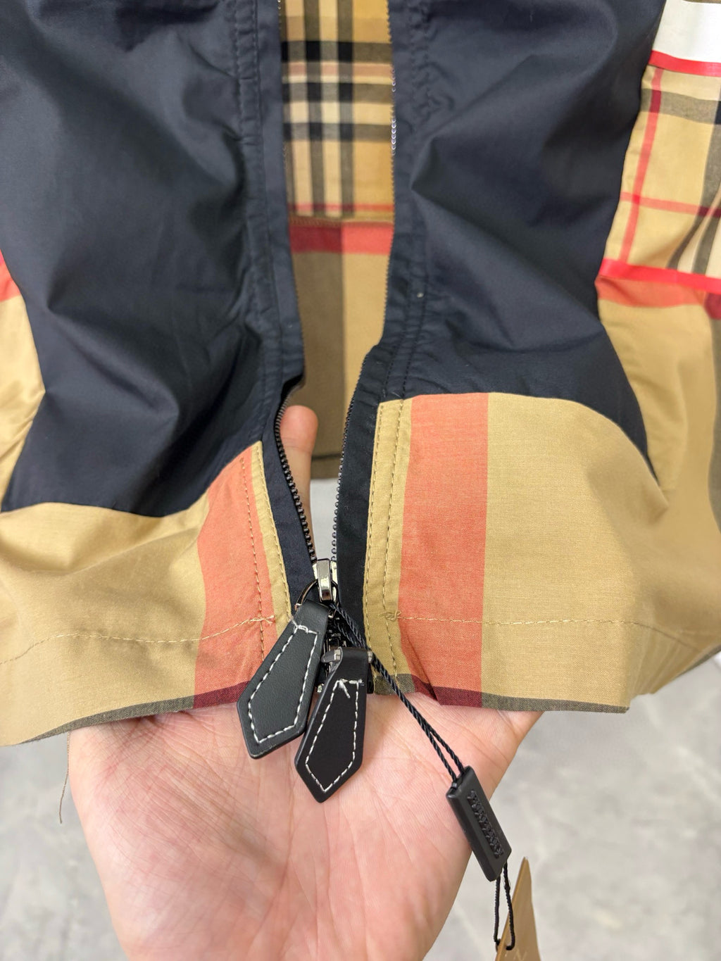 Burberry jacket zipper pull close-up on navy and beige plaid fabric