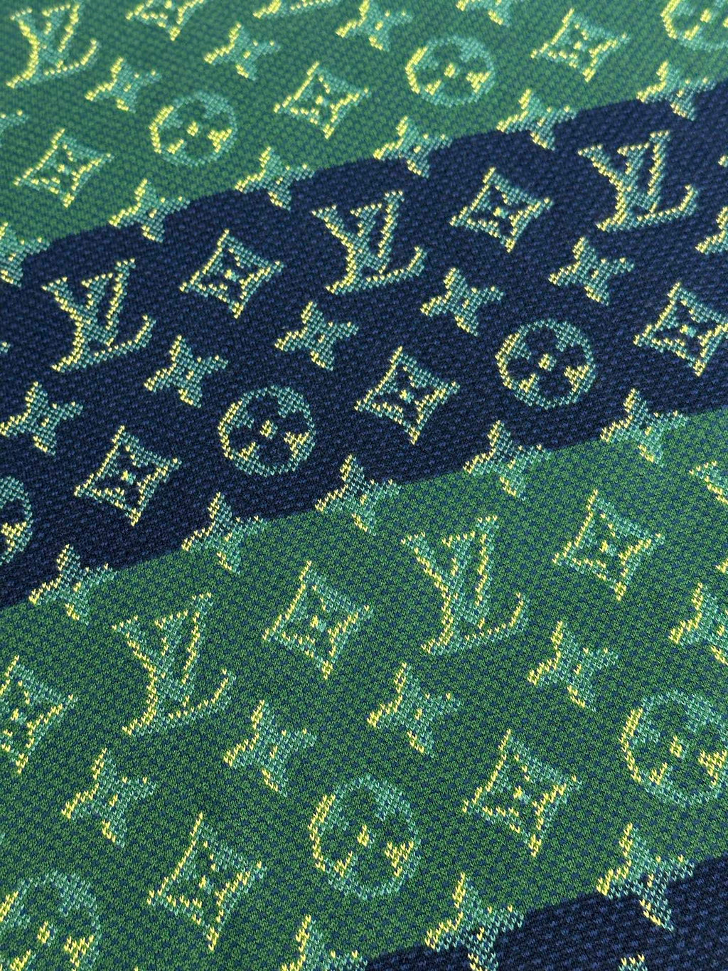 Close-up of textured knit fabric in green with navy and yellow monogram pattern