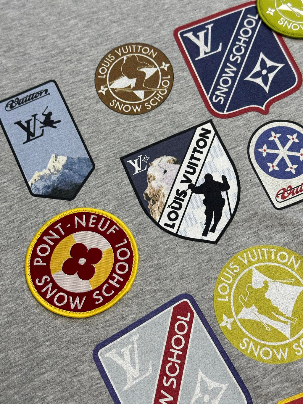 Light gray T-shirt with scattered embroidered logo patches and crew neck area