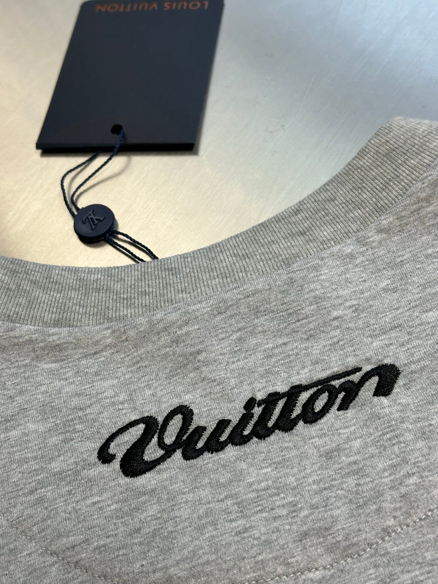 Grey T-shirt neckline with hanging tag and script logo graphic on chest