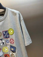 Grey T-shirt with close-up multi-logo patch detail on the chest