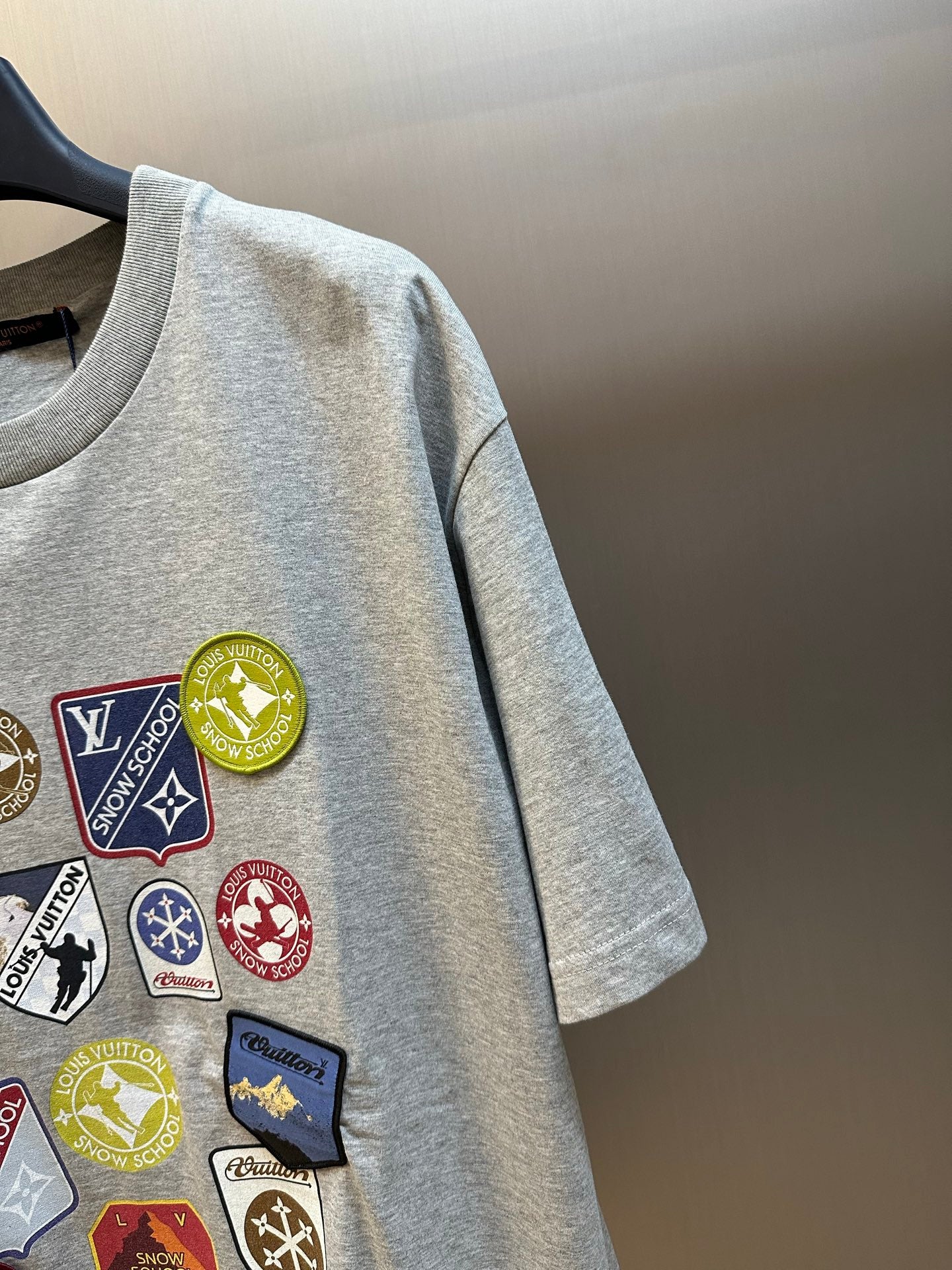 Grey T-shirt with close-up multi-logo patch detail on the chest