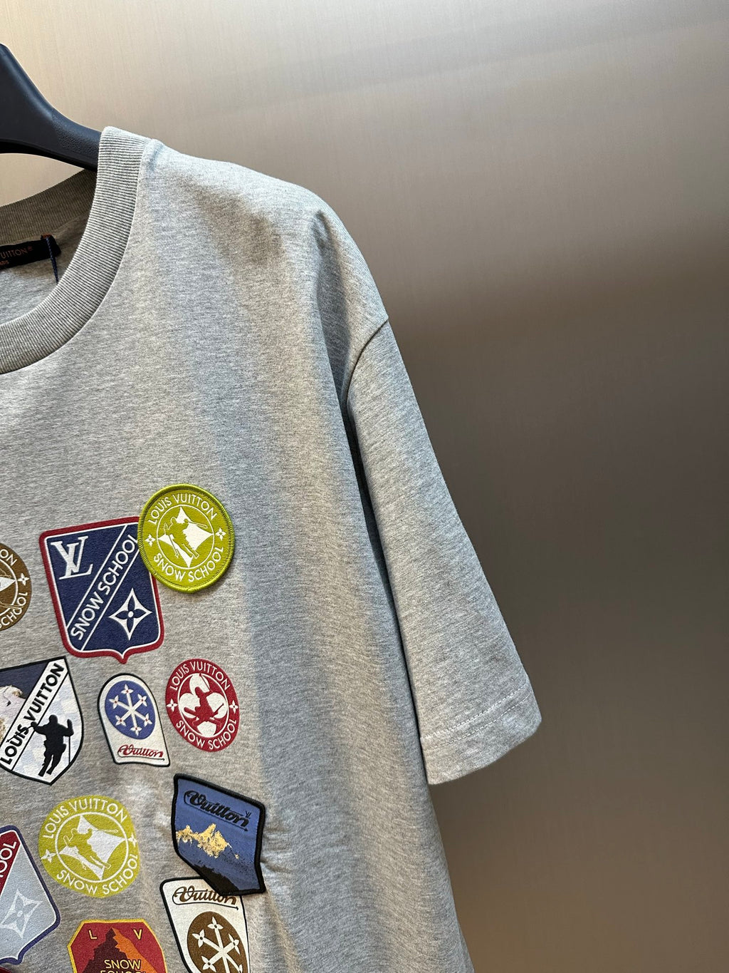 Light gray T-shirt sleeve with patch logo graphics near the shoulder