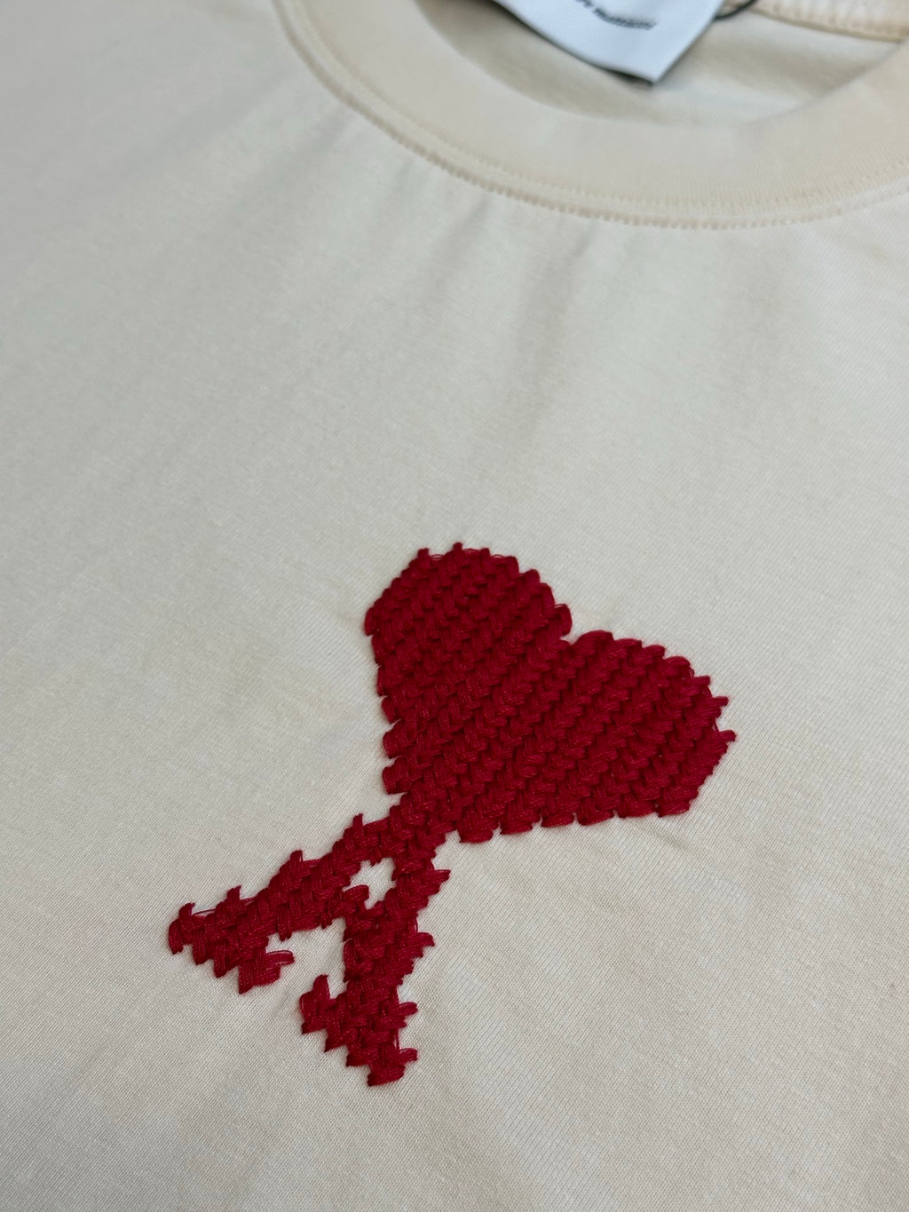 Red embroidered emblem on an off-white T-shirt front