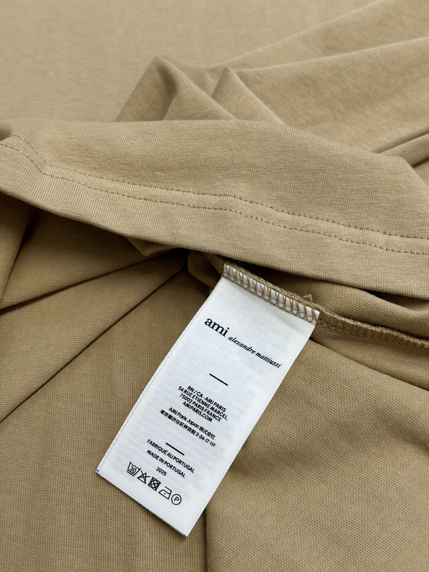 Amiri T-shirt light tan with white care label near folded fabric and hem
