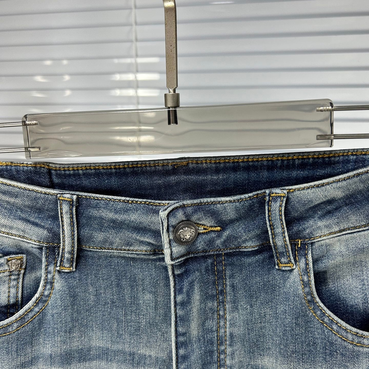 Denim jeans waistband with metal button and stitched logo patch at center
