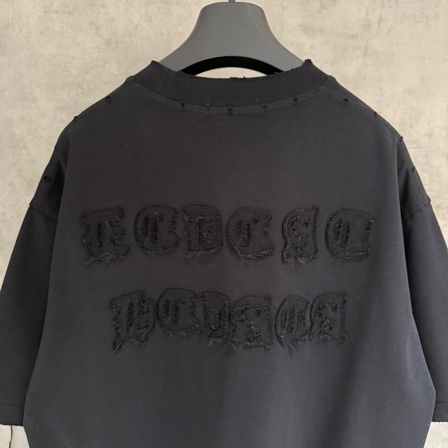 Black short-sleeve T-shirt with large embossed wordmark across upper back