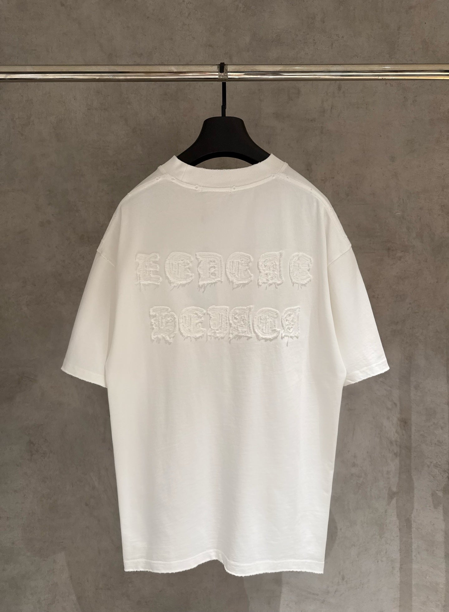 White crew-neck short-sleeve T-shirt with large raised embroidered logo on back.