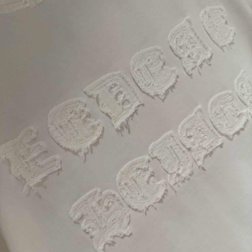 Raised embroidered logo detail on white T-shirt, showing textured stitching pattern.