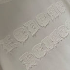 Raised embroidered logo detail on white T-shirt, showing textured stitching pattern.