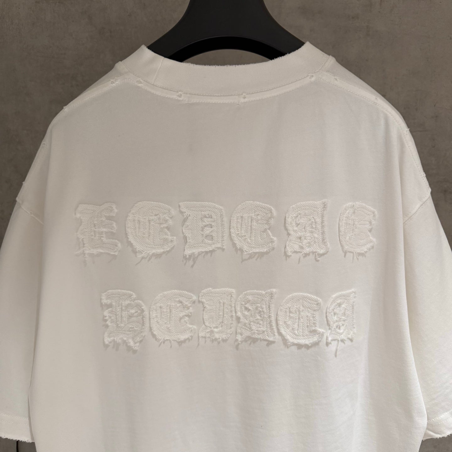 White crew-neck T-shirt with raised embroidered back logo, collar and hem visible.