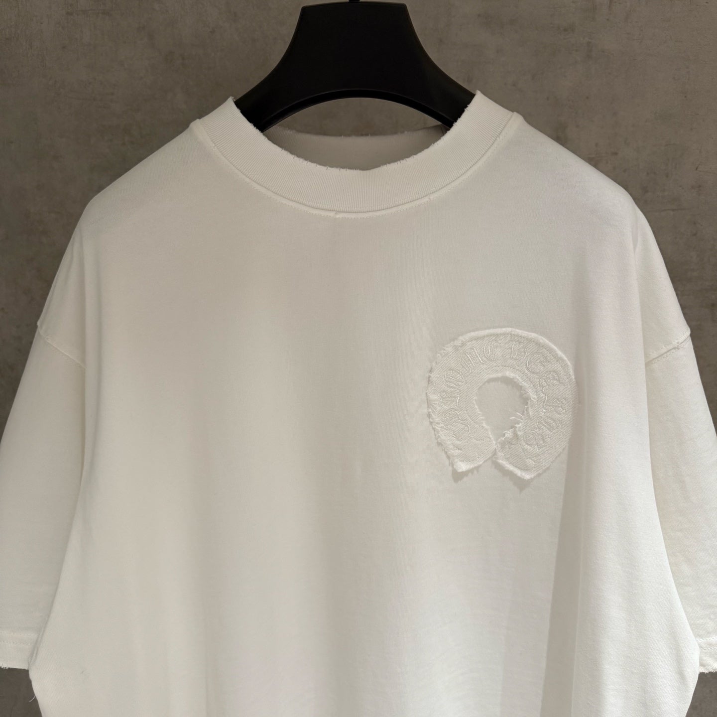 White crew-neck T-shirt with raised embroidered logo on left chest, close-up view.