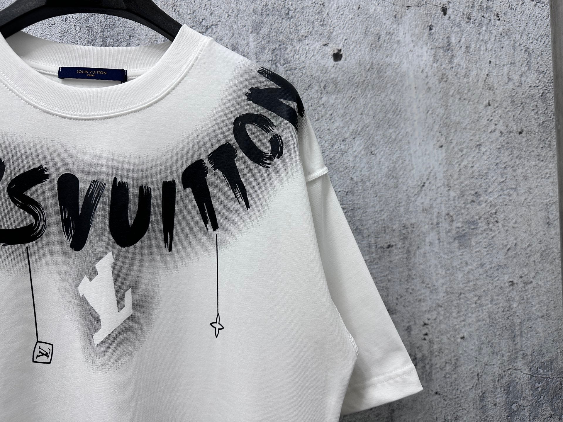 White T-shirt with close-up black “Louisvuitton” logo text and charm icons
