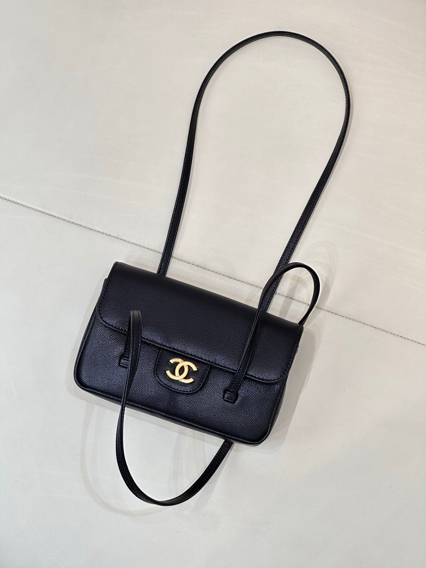Chanel handbag with flap front and gold CC logo, shown with long shoulder strap.