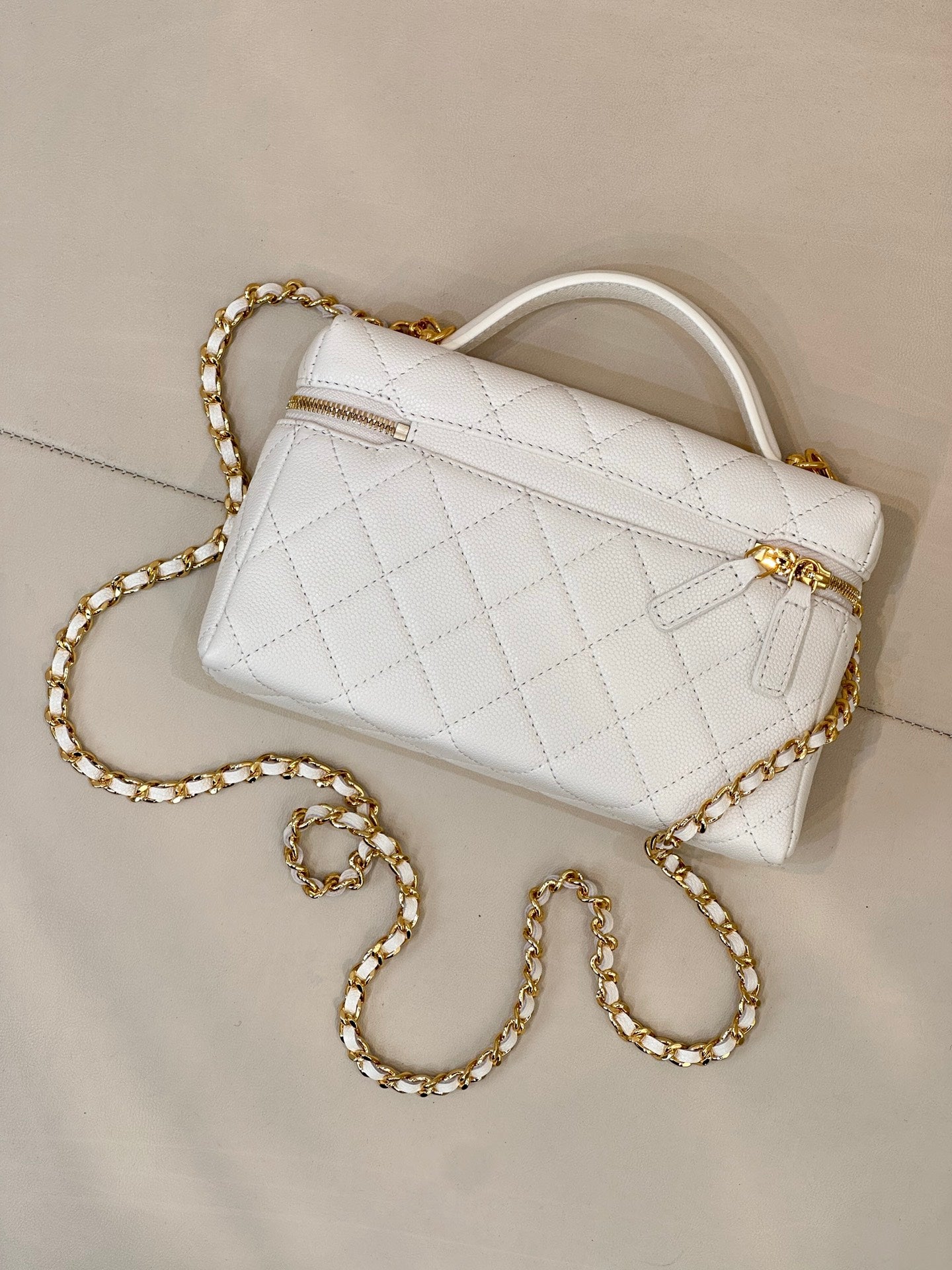 White quilted leather bag with top handle, gold hardware, and long gold chain strap.