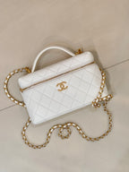 White quilted leather crossbody bag with top handle and gold chain strap.