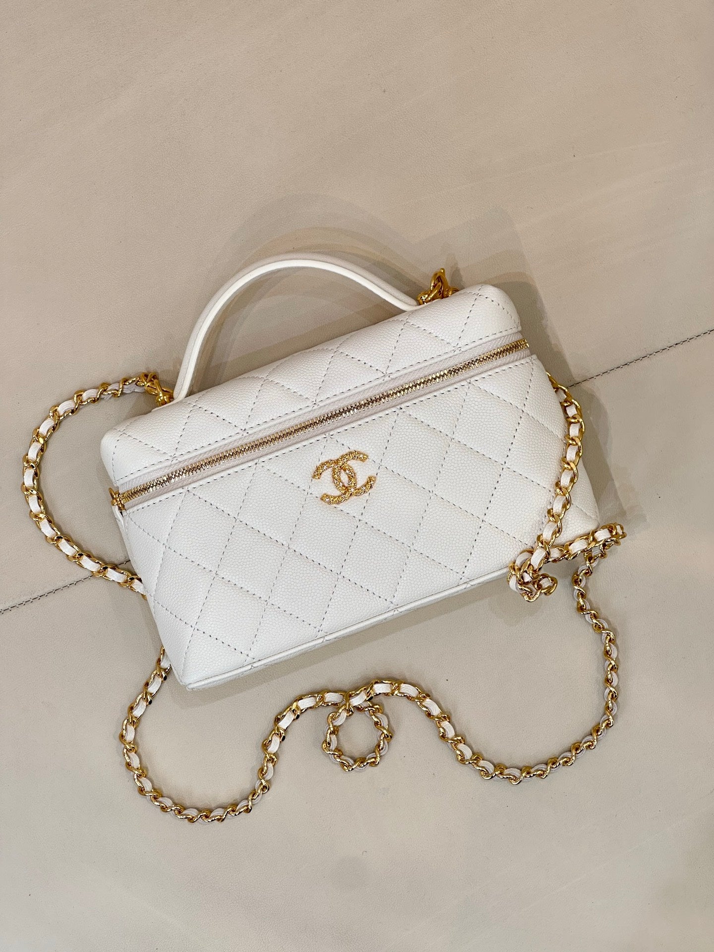 White quilted leather crossbody bag with top handle and gold chain strap.