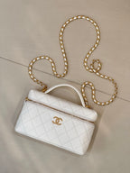 White quilted leather handbag with top handle, zip pocket, and gold chain strap.