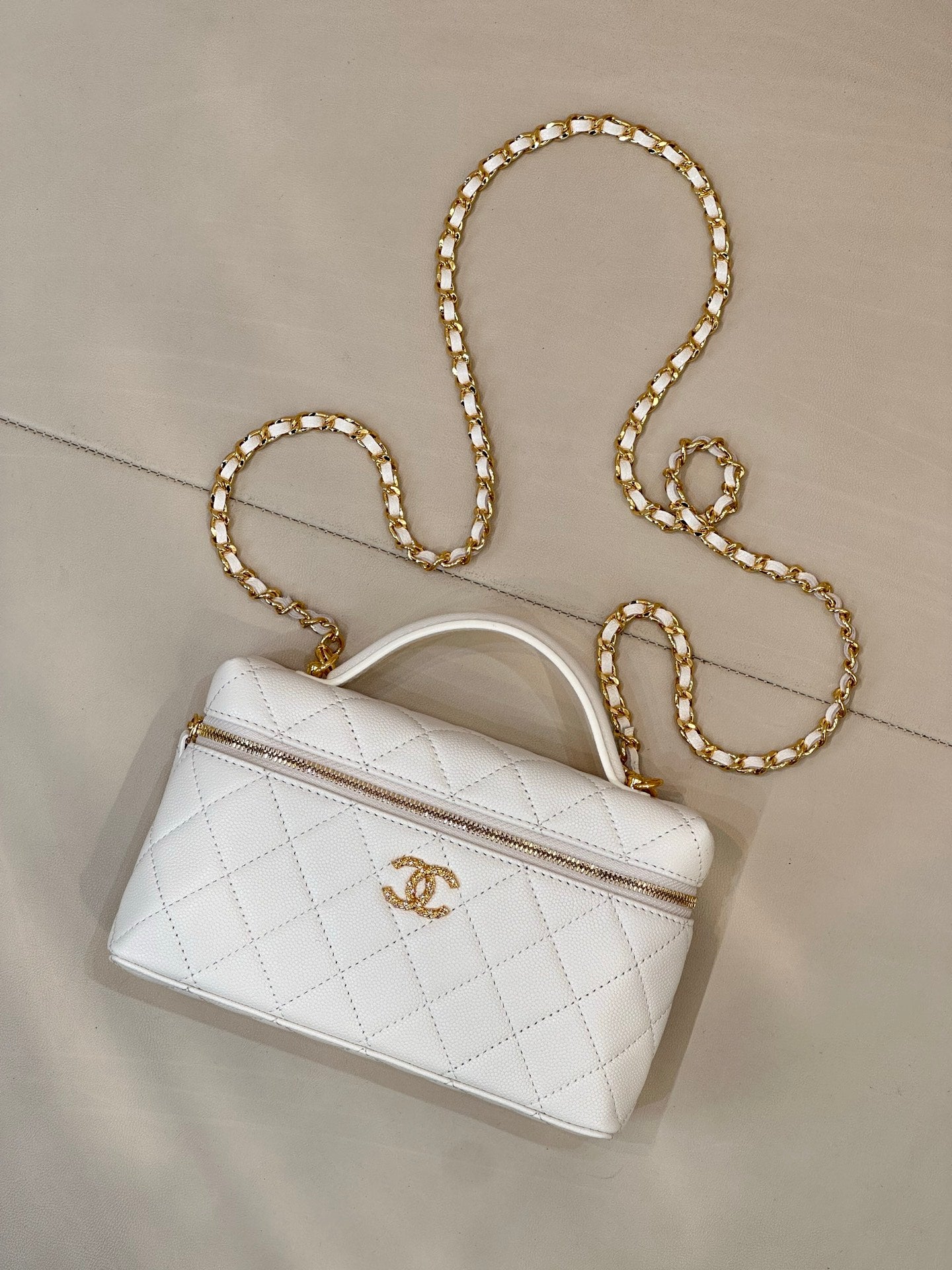 White quilted leather handbag with top handle, zip pocket, and gold chain strap.