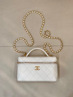 White quilted leather bag with top handle, zip closure, and gold chain strap.