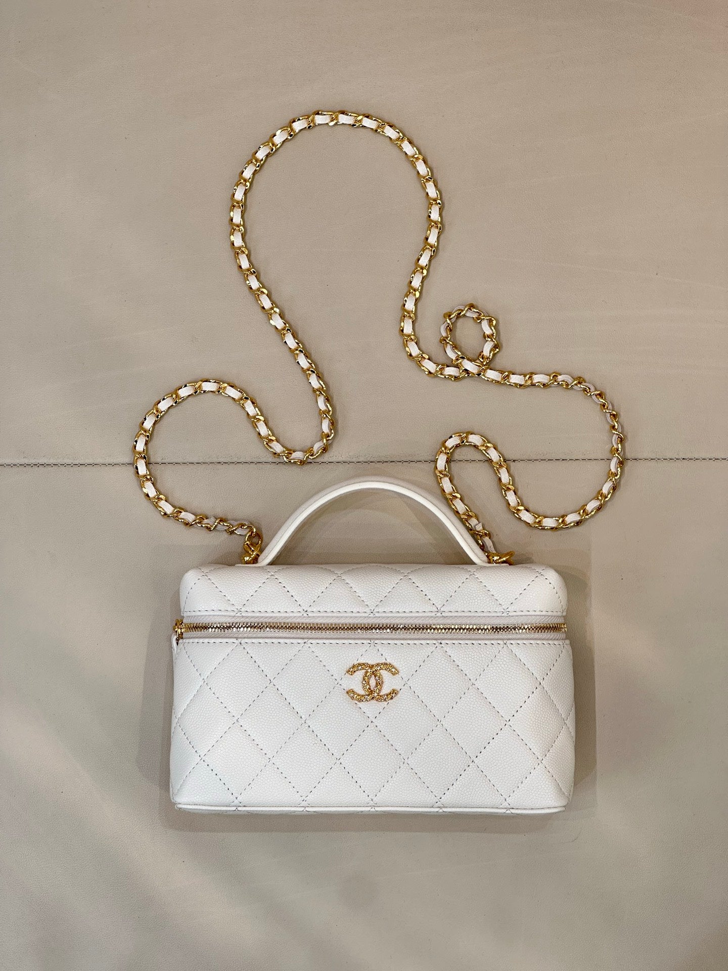 White quilted leather bag with top handle, zip closure, and gold chain strap.