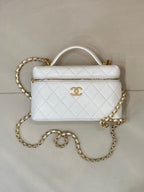 White quilted leather bag with top handle, gold zipper trim, and gold chain strap.