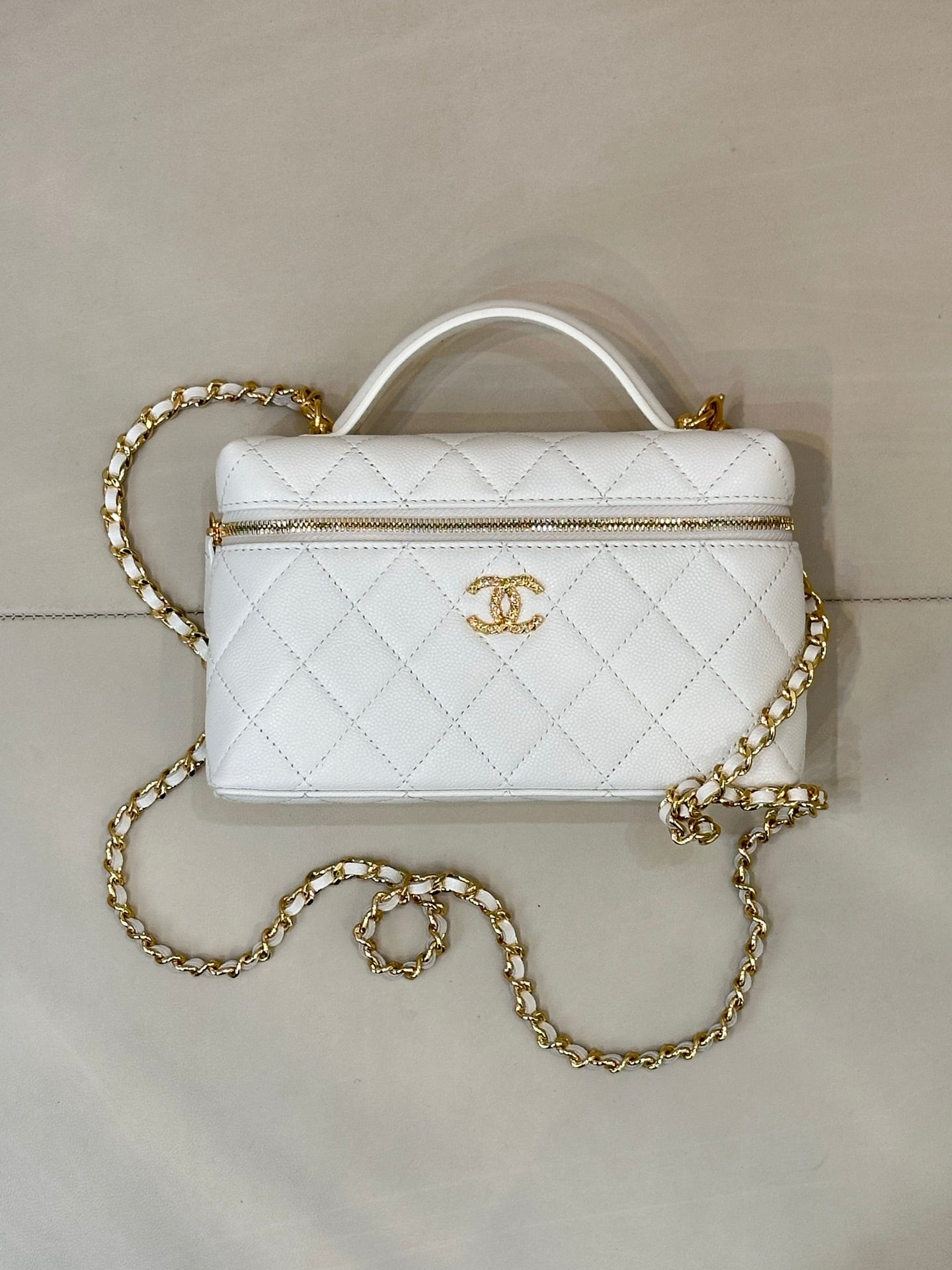 White quilted leather bag with top handle, gold zipper trim, and gold chain strap.