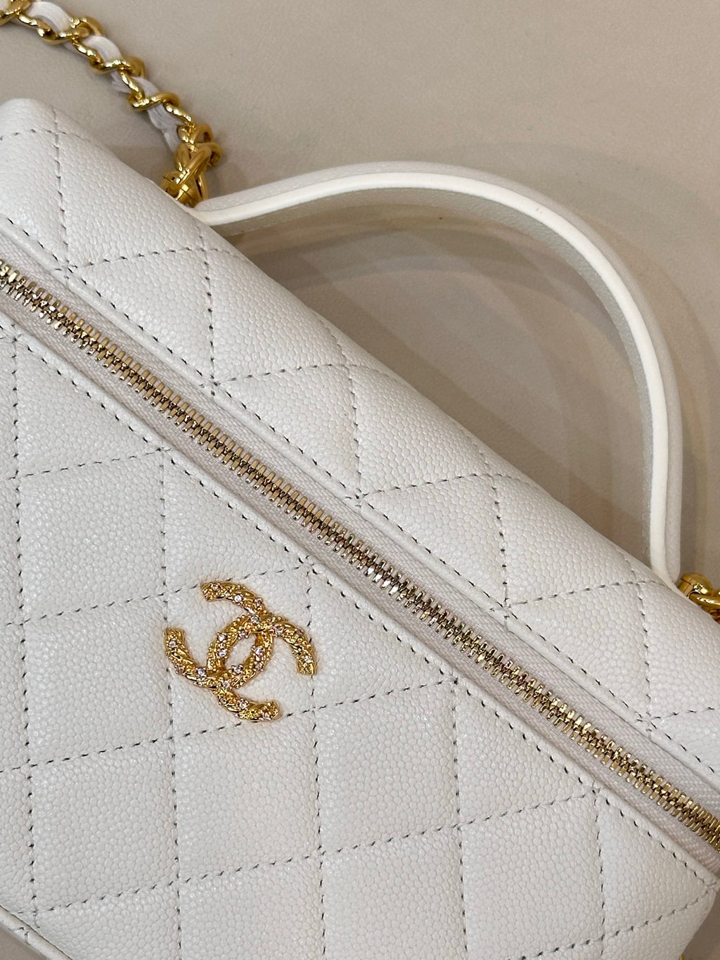 White quilted leather bag panel with gold zipper and gold logo detail.