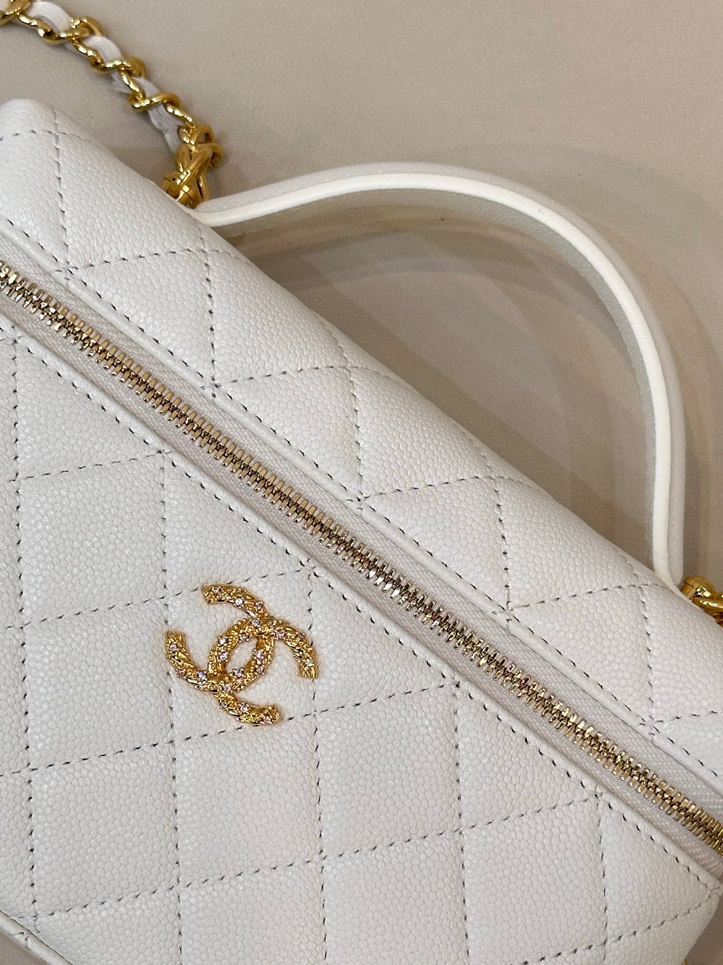 White quilted leather bag panel with gold zipper and gold logo detail.