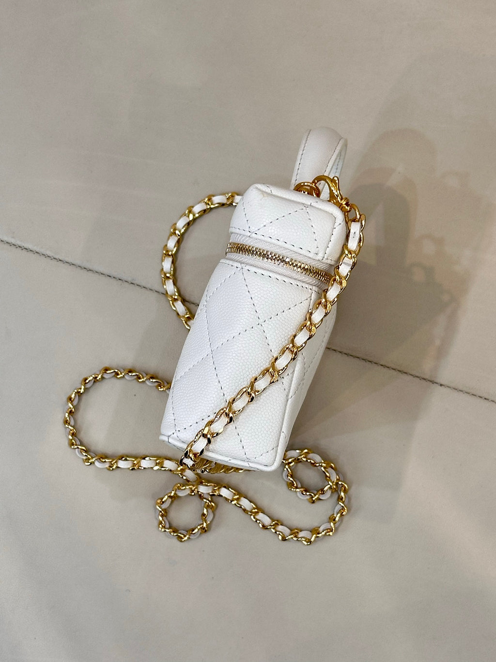 White quilted leather bag side view with gold chain strap and top handle.