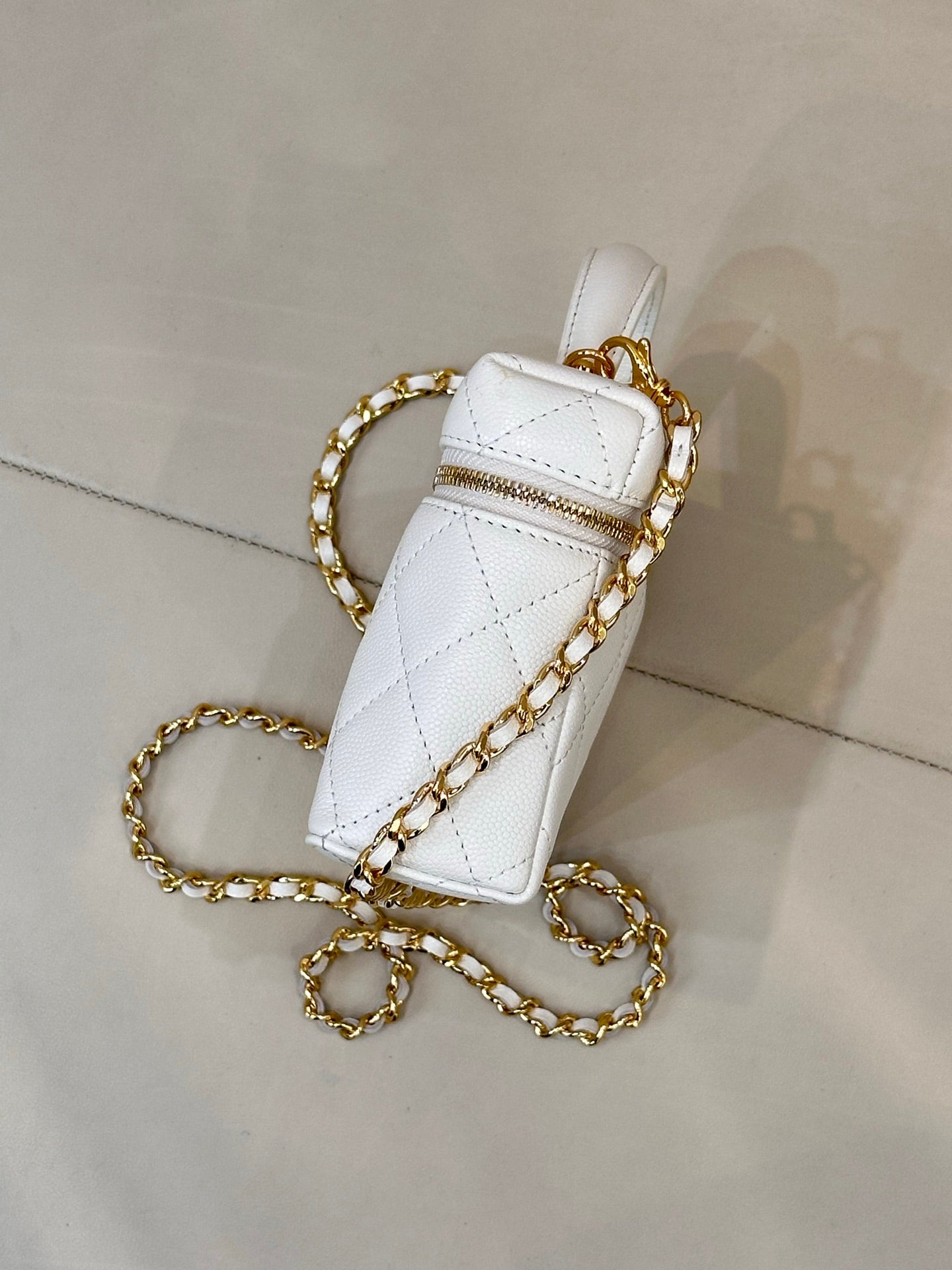 White quilted leather bag side view with gold chain strap and top handle.