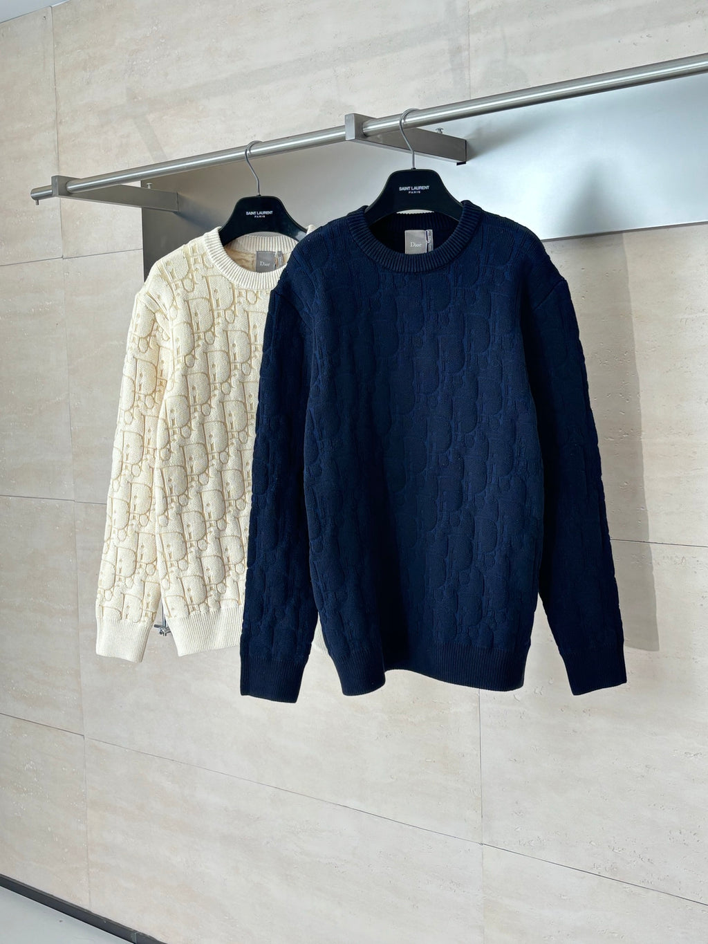 Dark navy cable-knit sweater on hanger next to cream sweater.