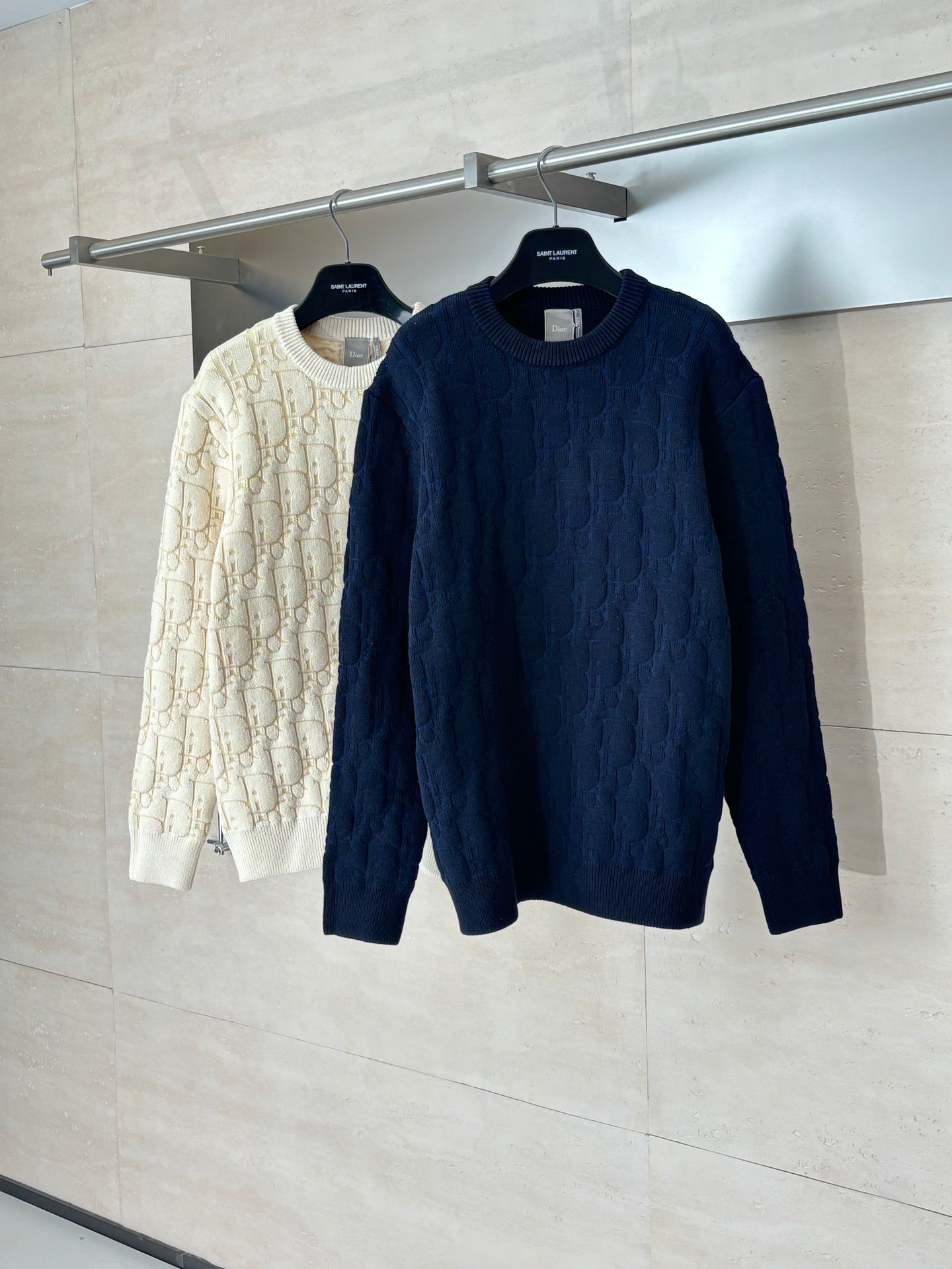 Dark navy cable-knit sweater on hanger next to cream sweater.