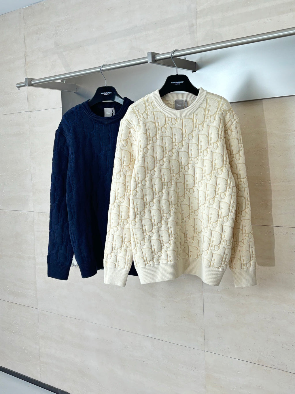 Cream and navy knit sweaters on hangers, both with allover Dior-style logo pattern