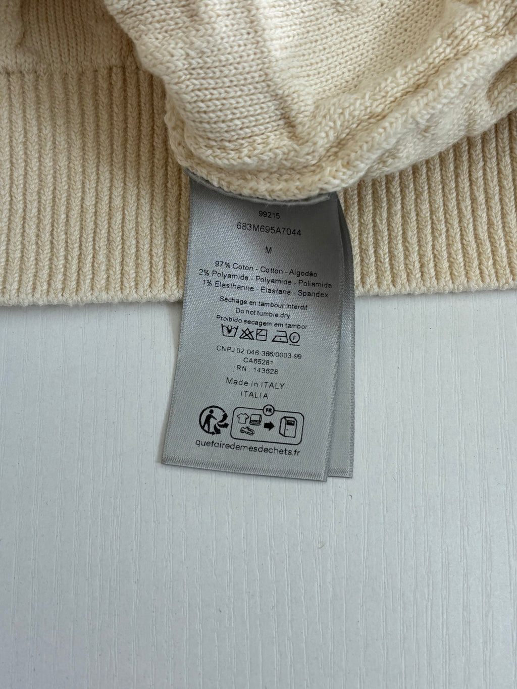 Cream knit sweater fabric with attached care label tag at the hem