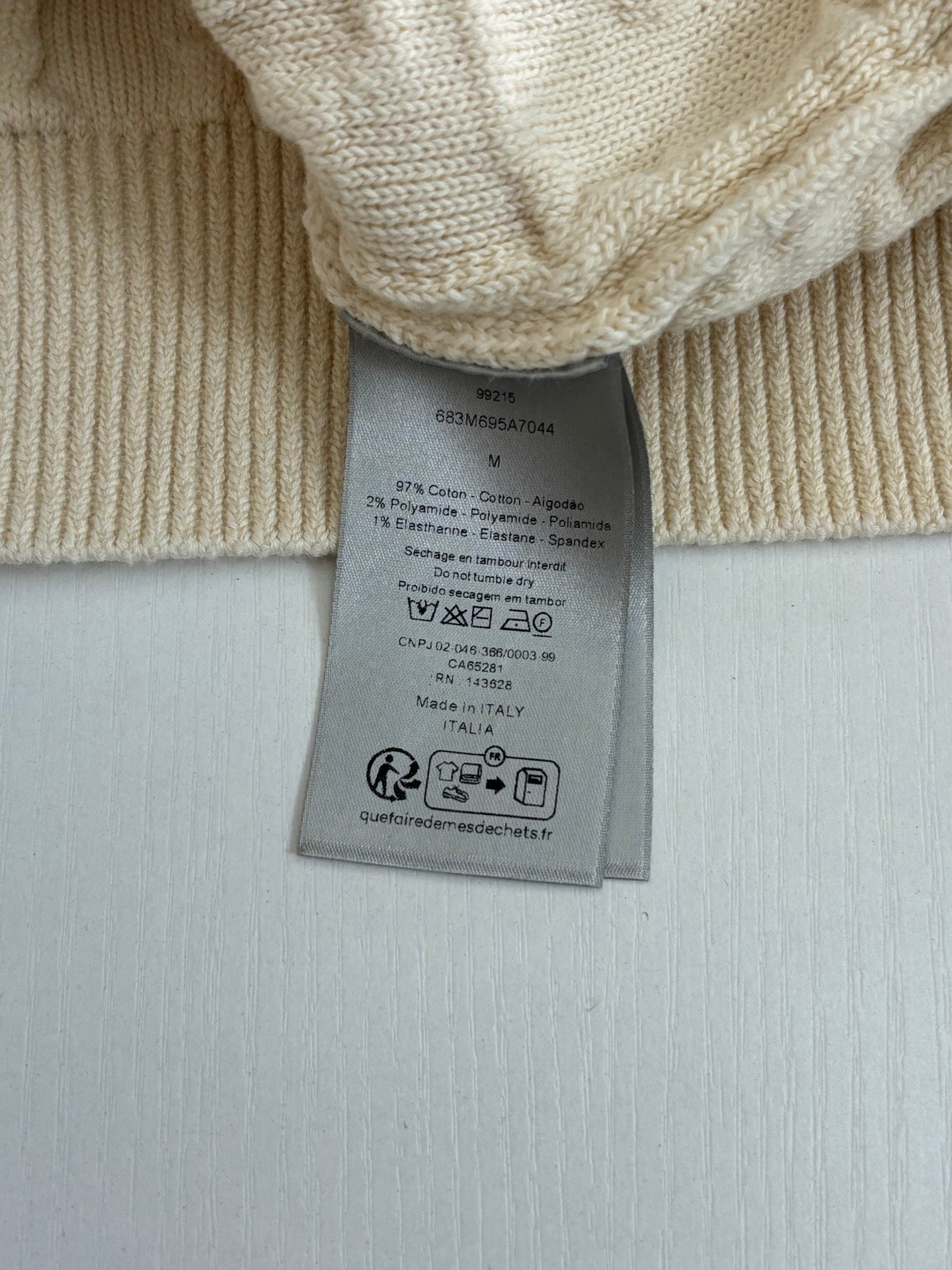 Cream knit sweater fabric with attached care label tag at the hem