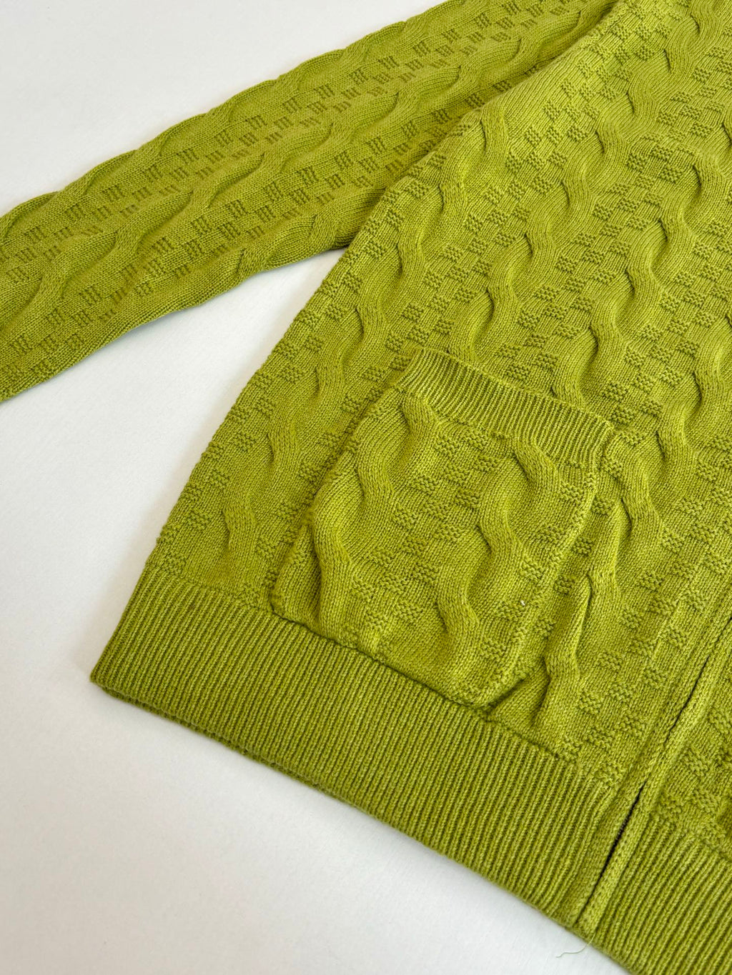 Green knit sweater sleeve with textured cable pattern and ribbed cuff