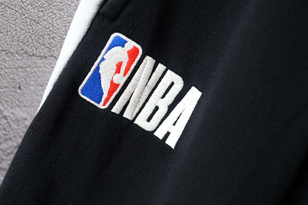 Black Balenciaga pants with colorful “NBA” logo patch